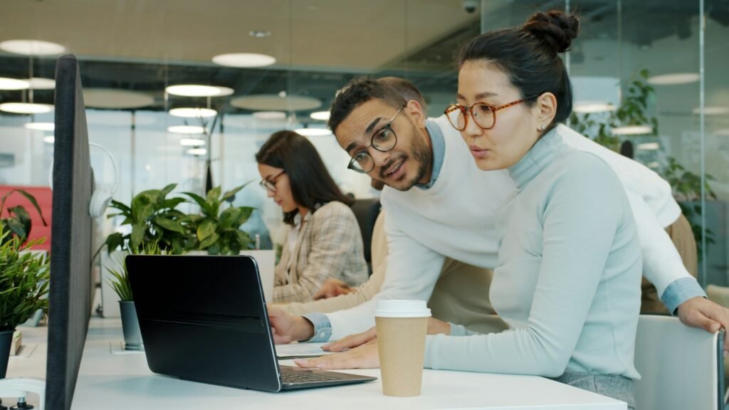 Two coworkers reviewing information on a laptop at an office desk.